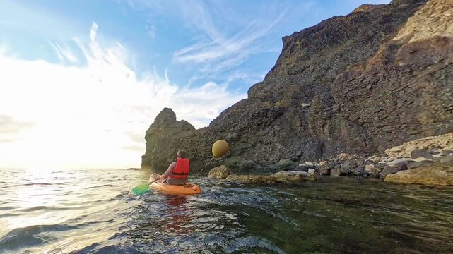 Kayaking ocean coastline man paddling orange kayak along rocky cliffs during beautiful sunset for adventure and summer vacation