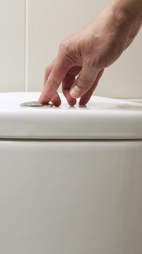 Closeup of female hand pushing a button to flush a close tool a bathroom toilet at home