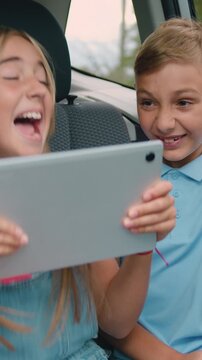 Children boy and girl sit in car using digital tablet for games and entertainment, celebrate vin and give high fives traveling by car. Concept of a family holiday. Slow motion.