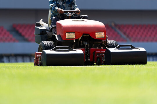 Workers are using a lawnmower to maintain the football pitch