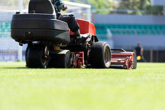 Workers are using a lawnmower to maintain the football pitch