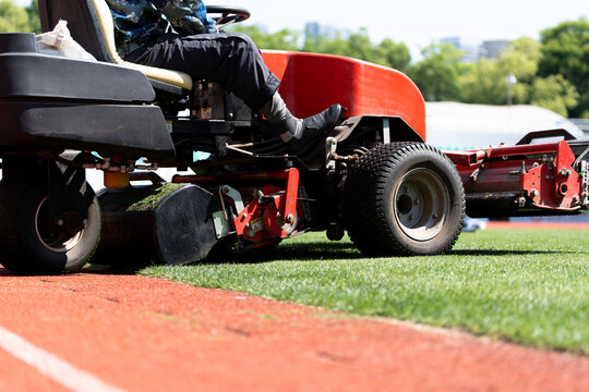 Workers are using a lawnmower to maintain the football pitch