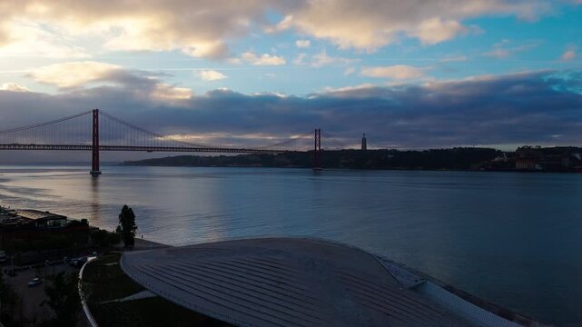 Aerial reveal of MAAT museum rooftop and 25 de Abril Bridge over Tagus River at sunrise in Lisbon Portugal