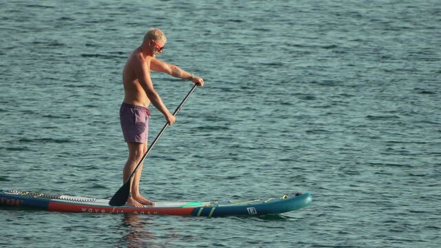 Man paddleboarding in ocean, enjoying water sports on a calm sunny day, summer activity vacation