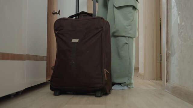 Caucasian woman pausing beside suitcase hallway, tense pause at threshold with hands on handle, green cargo pants and casual socks, closeup on fingers and fabric, seated moment of introspection
