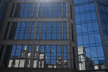 Obraz premium Reflection of historic architecture in a modern glass building facade on a clear day.