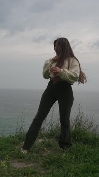 Woman dancing cliff young woman with long hair dances on a grassy cliff overlooking the ocean during a cloudy day