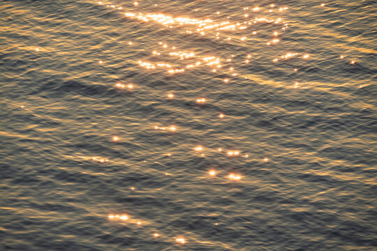 Beautiful golden sunlight reflecting on the rippling surface of the Baltic Sea during sunset, creating a shimmering water texture.
