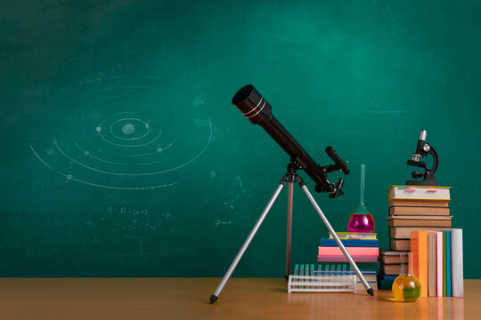 Natural sciences classroom scene with telescope, textbooks, microscope and chemistry glassware against green chalkboard. Blank space for text.
