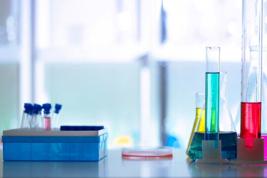 Blurred background with medical laboratory glassware with colorful liquid samples in test tubes and measuring cylinders, shallow depth, clinical testing concept.