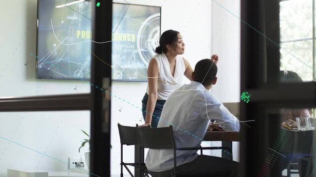 Female colleague leaning over laptop in business meeting, pointing at animated chart, guiding man