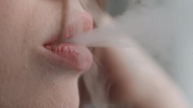 Closeup lips using vape device, soft exhale of vapor in muted window light intimate portrait of contemplative person pausing in apartment, visible pod and mouth detail, subtle skin texture