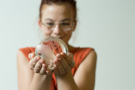 Young woman with glasses gently holding a glass globe showing continents
