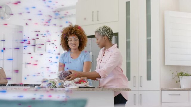 Two women reaching mesh bag, passing grapes, preparing meal while particles passing across left