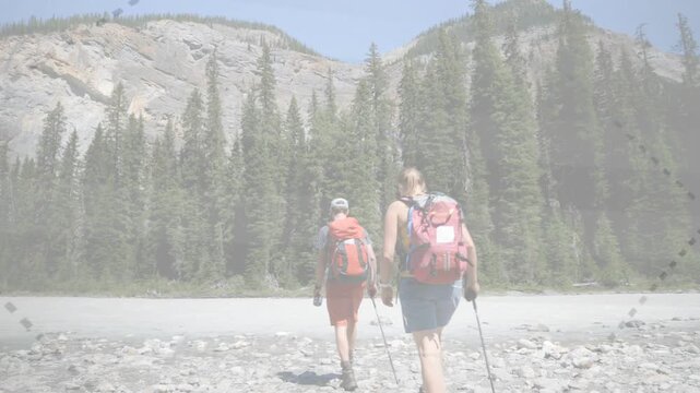 Right-edge entering two hikers walking toward trees on rocky shore carrying water,pole for health
