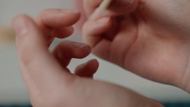 Closeup hands prepping nails with spatula, wooden tool used to push cuticles, precise motions, clean studio lighting, steady technician hands, careful finish and polish preparation