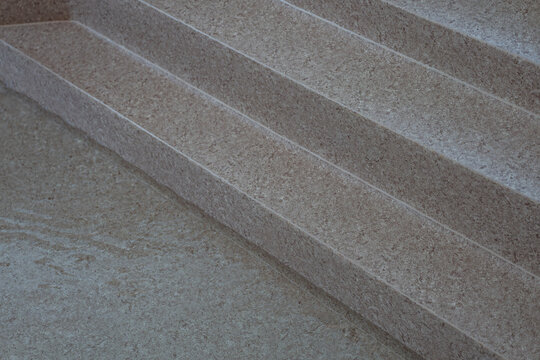 Vue en diagonale d'une s&eacute;rie de marches en b&eacute;ton &agrave; la texture granuleuse, formant un motif g&eacute;om&eacute;trique minimaliste et &eacute;pur&eacute; sous une lumi&egrave;re uniforme.