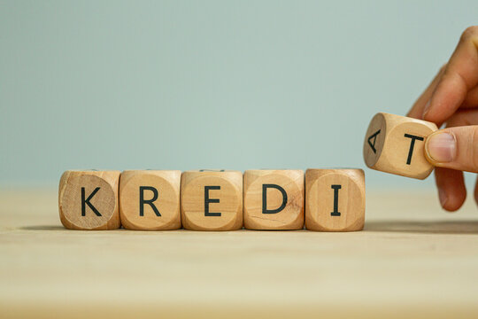 A hand manipulates wooden blocks with letters spelling out credit