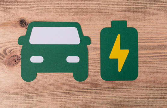 Electric vehicle and charging concept with car icon and battery sign on wood.  Sustainability and ec
