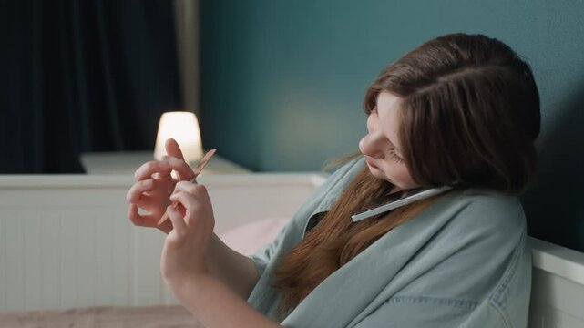 Soft evening portrait of woman inspecting fingertips by bedside lamp, teal wall and cozy bedding set an intimate, contemplative atmosphere slow camera captures subtle smile, gentle motion and personal