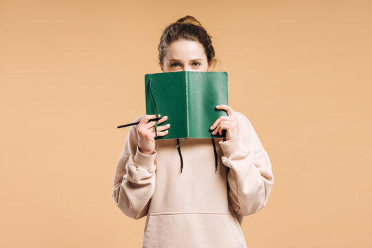 Young woman hiding face behind green notebook