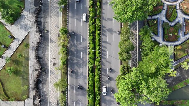 A view from above of an urban boulevard with a green median, traffic, and pedestrians along the sidewalk in a park in the city of Pontianak, Indonesia.