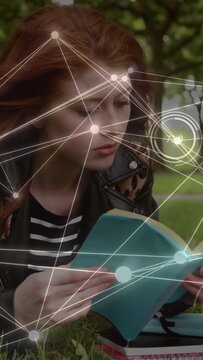 Vertical video: Woman reading teal book in park opening pages to study as HUD overlaying around her