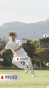 Vertical video: Male cricketer chasing incoming red ball, diving and rolling to catch amid badges