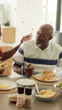 Vertical video: Senior man turning as son nudging arm offering sandwich, gold stars marking food