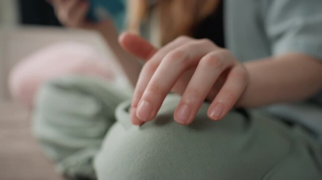 Caucasian girl mindful hand resting on knee while holding tablet, gentle fingertip tapping and slow breath, textured cushion and relaxed domestic setting, subtle motion and self soothing focus