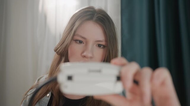 Caucasian woman inspecting blood pressure monitor up close in bedroom curtain backdrop, home vlogger testing cuff device, medical student practice scene, focused expression and subtle worry, soft