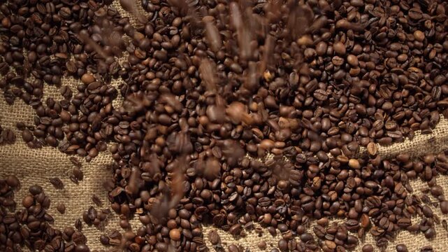 Top view of freshly roasted coffee beans falling in motion onto rustic burlap fabric pile creating dynamic heap for artisan cafe menu background organic agriculture harvest and trade