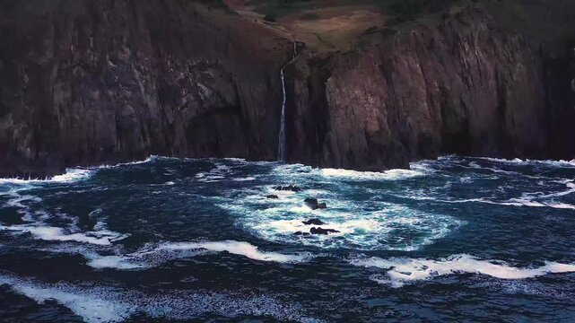 Aerial view of Mealt Falls plunging from Kilt Rock cliffs into the ocean in Scotland