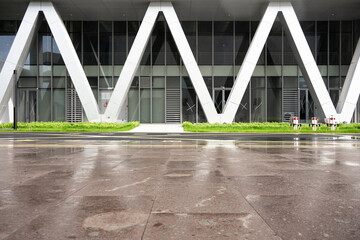 Naklejka premium Modern architectural facade with V-shaped columns and wet plaza ground after rain