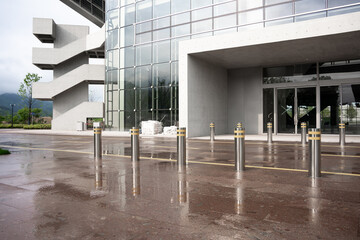 Naklejka premium Modern glass curtain wall building entrance after rain with wet reflective pavement and bollards