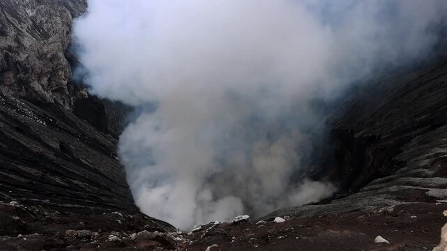 A powerful view looking down into an active volcanic crater, where thick white steam billows upward from deep within the vent.Mount Bromo in East Java, Indonesia