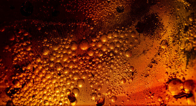 Macro shot of refreshing cola drink with ice cubes and fizzy bubbles in a glass with water drops.