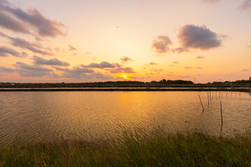 Obraz premium Colorful Sunset Sky Over Serene Water and Coastline,A beautiful sunset illuminates the clouds in vibrant orange and pink hues over a calm body of water. The setting sun casts a warm glow, reflecting.