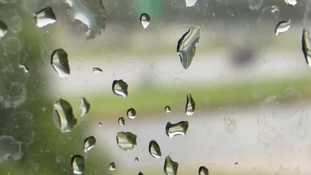 Rain drops on glass with traffic passing by 
