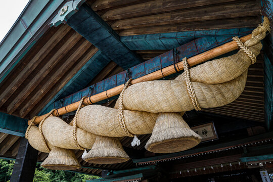 日本の伝統的な神社に飾られた重厚で巨大な注連縄（しめなわ）と社殿の屋根