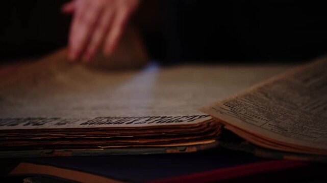 Person flipping through pages of an old book in a dimly lit room.