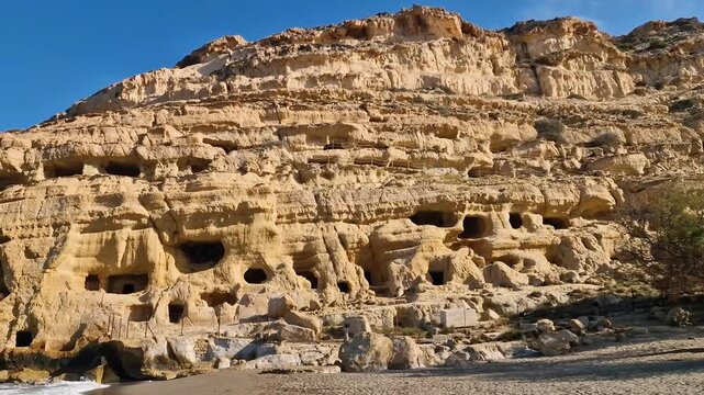 Morning at empty Matala beach with ambient sound of waves, Crete. Scenic view of ancient caves and Libyan sea at dawn with no people. Authentic Mediterranean nature and relaxing sea noise, 4k.