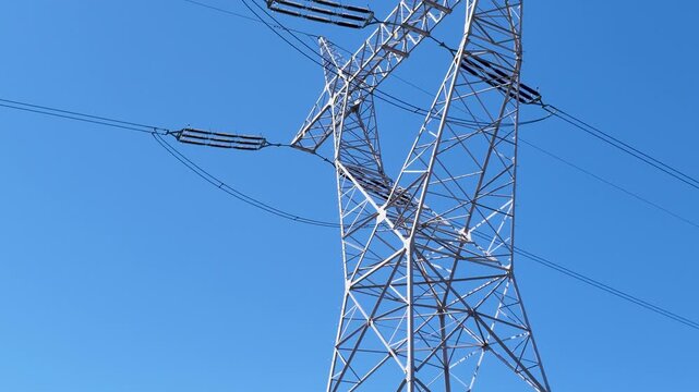 High voltage power line pylon against clear blue sky, low angle view of electrical grid infrastructure for renewable energy distribution and smart city power management systems.