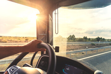 Close view of truck driver hand on steering wheel with road and warm sunlight © M. Perfectti