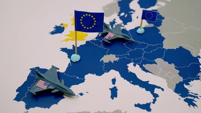 Hand removing toy fighter jets with American flags from a map of Europe, symbolizing the withdrawal of United States military troops and a shift in geopolitical strategy and defense policy