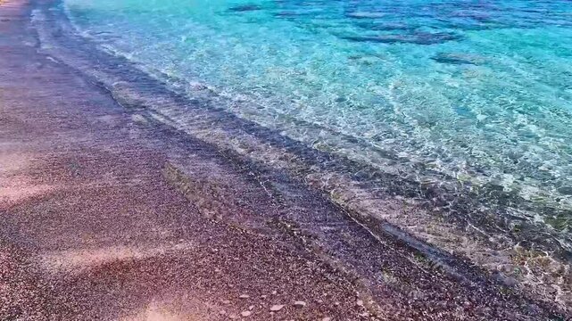 Elafonisi beach with pink and black sand in Crete, Greece. Close up of turquoise sea waves with original sound of nature. Exotic wild beach contrasts, crystal clear water. Summer travel, 4k.