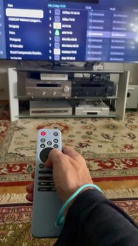 Mando televisi&oacute;n, plataforma digital y canales con mano haciendo zapping smart tv en pantalla en control remoto con aplicaci&oacute;n en sal&oacute;n de casa
