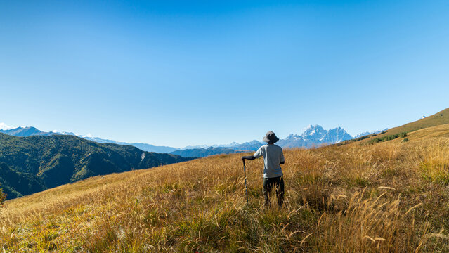 Traveler standing in tall grass enjoying the view of Mount Ushba near Mestia, Svaneti, Georgia. Mountain adventure and outdoor nature exploration.
