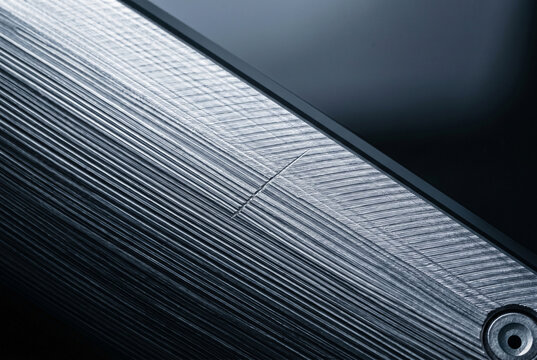 A geometric macro abstraction of high-contrast ridges and valleys on precision-milled aluminum at the sharp interface where the technical grey metal meets the dark glass top.