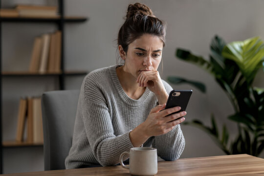 Woman reading message on smartphone with worried expression, thinking before replying, communication and relationship tension concept
